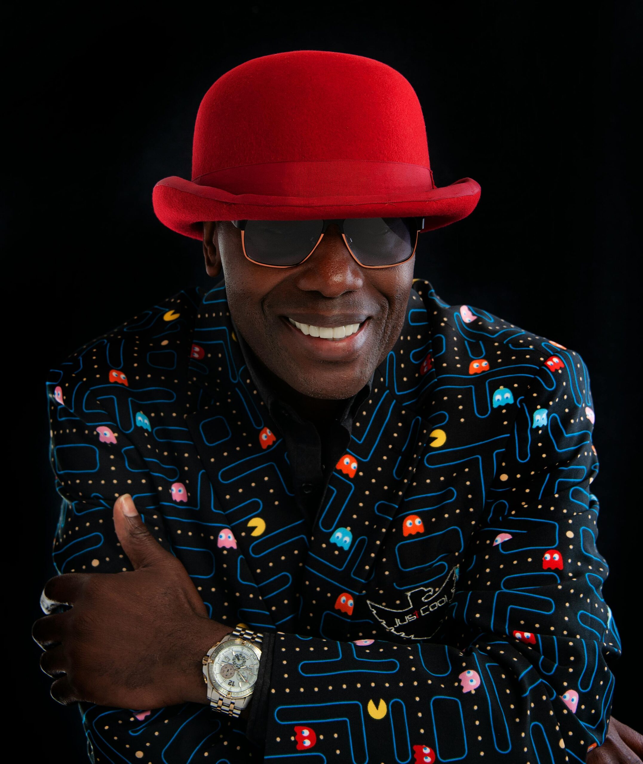Man wearing a bold red hat with a Pac-Man patterned blazer, exuding confidence.